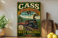 A vintage-style metal sign for Cass Scenic Railroad, featuring a train on a track through a forested mountain landscape.