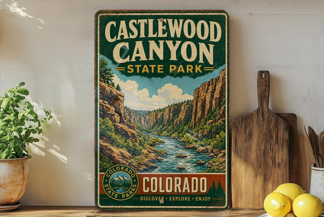 A vintage-style sign for Castlewood Canyon State Park, featuring a scenic illustration of the canyon landscape with a river flowing through it. The sign is displayed on a shelf next to a wooden cutting board and some potted plants.
