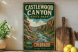A vintage-style sign for Castlewood Canyon State Park, featuring a scenic illustration of the canyon landscape with a river flowing through it. The sign is displayed on a shelf next to a wooden cutting board and some potted plants.