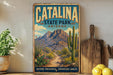 A vintage-style metal sign for Catalina State Park in Arizona, featuring a desert landscape with mountains, cacti, and a path leading to the park.