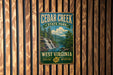 A vintage-style metal sign for Cedar Creek State Park in West Virginia, featuring a scenic image of a waterfall and forest.