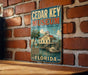A vintage-style sign for the Cedar Key Museum in Florida, featuring an illustration of a building with a palm tree and a boat on the water.