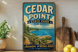 A vintage-style metal sign for Cedar Point State Park in New York, featuring a scenic illustration of the park's landscape with a wooden walkway leading to a lake.