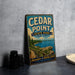 A vintage-style metal sign for Cedar Point State Park in New York, featuring a scenic image of the park and a path leading to a lake.