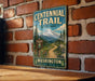 A vintage-style metal sign for Centennial Trail, located in Washington State Park, with a mountain landscape and trail sign.