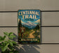 A vintage-style metal sign for Centennial Trail, located in Washington State Park, with a mountain landscape and trail sign.