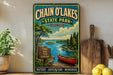 A vintage-style metal sign for Chain O'Lakes State Park in Illinois, featuring a scenic image of a lake, canoe, and forest.