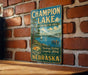 A vintage-style metal sign for Champion Lake, the state recreation area in Nebraska, featuring a scenic image of a lake with boats and people enjoying the outdoors.