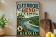 A vintage-style metal sign for Chattanooga Bend State Park in Georgia, featuring a scenic landscape with a river and pine trees.