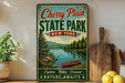 A vintage-style sign for Cherry Plain State Park in New York, featuring a scenic image of a lake with a canoe, surrounded by pine trees and mountains.