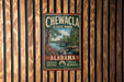 A vintage metal sign for Chewala State Park in Alabama, featuring a scenic landscape with a river, bridge, and trees.