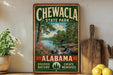 A vintage-style sign for Chewala State Park in Alabama, featuring a scenic landscape with a river, bridge, and trees.