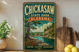 A vintage-style sign for Chickasaw State Park in Alabama, featuring a scenic landscape with a river, trees, and a house.
