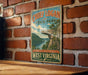 A vintage-style sign for Chief Logan State Park, featuring a scenic landscape with a river and mountains, mounted on a brick wall.