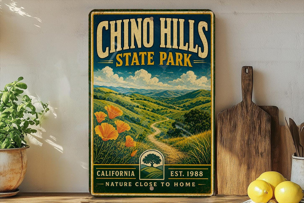 A vintage-style metal sign for Chinook Hills State Park, featuring a scenic landscape with mountains, hills, and a winding path.
