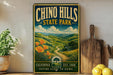 A vintage-style metal sign for Chinook Hills State Park, featuring a scenic landscape with mountains, hills, and a winding path.