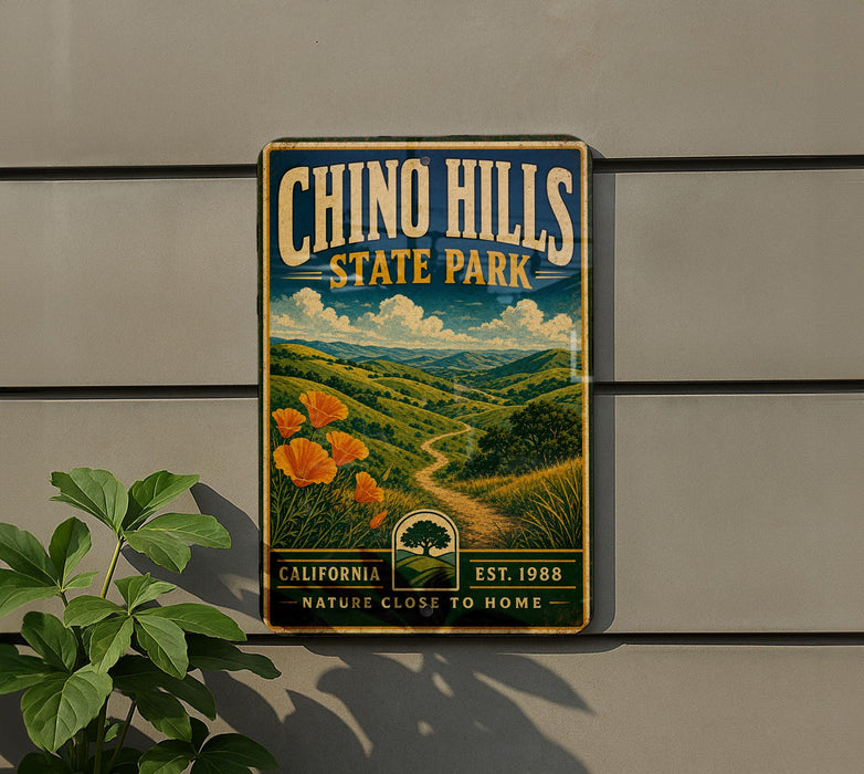 A vintage-style metal sign for Chino Hills State Park, featuring a scenic landscape with a winding path and orange flowers.