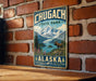 A vintage metal sign for Chugach State Park in Alaska, featuring a mountain landscape with a moose in the foreground.
