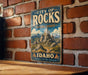 A vintage-style metal sign for the City of Rocks National Reserve in Idaho, featuring a mountain landscape and the text "Idaho" and "Discover a 'Tinless' Landscape".