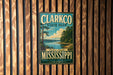 A vintage-style metal sign for Clarkco State Park in Mississippi, featuring a scenic landscape with a lake and trees.