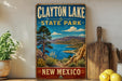A vintage-style sign for Clayton Lake State Park in New Mexico, featuring a scenic landscape with mountains, a lake, and desert vegetation.
