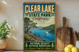 A vintage-style sign for Clear Lake State Park, California, featuring a scenic landscape with a lake, mountains, and sailboats.