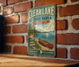 A vintage metal sign for Clear Lake State Park in Michigan, featuring a scenic illustration of a lake, canoe, and surrounding forest.