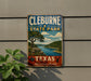 A vintage metal sign for Cleburne State Park in Texas, featuring a scenic landscape with a river and trees.