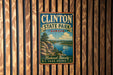 A vintage metal sign for Clinton State Park in Kansas, featuring a scenic landscape with a lake, mountains, and a sailboat.
