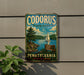 A vintage metal sign for Codorus State Park in Pennsylvania, featuring a scenic image of a lake with a sailboat and mountains in the background.