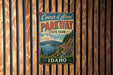 A vintage metal sign for Coeur d'Alene Parkway, featuring a scenic mountain landscape and a winding road.