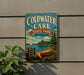 A vintage metal sign for Coldwater Lake State Park in Michigan, featuring a scenic illustration of a lake, boat, and forest.