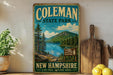 A vintage-style sign for Coleman State Park in New Hampshire, featuring a scenic landscape with pine trees, a lake, and mountains.