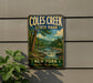 A vintage-style metal sign for Coles Creek State Park, featuring a scenic landscape with a river, trees, and mountains.
