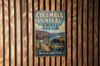 A metal sign for Columbia Plateau Trail in Washington State Park, featuring a scenic image of the trail and the words "Columbia Plateau Trail" and "State Park Washington".