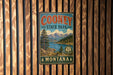 A vintage-style metal sign for Cooney State Park in Montana, featuring a scenic landscape with mountains, trees, and a lake.