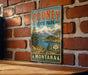 A vintage-style metal sign for Cooney State Park in Montana, featuring a scenic landscape with mountains, trees, and a lake.