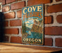 A vintage metal sign for Cove Palisades State Park in Oregon, featuring a scenic mountain landscape with a lake and pine trees.