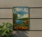 A vintage-style sign for Cowan Lake State Park in Ohio, featuring a scenic landscape with a lake, trees, and mountains.