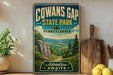 a vintage-style sign for Cowans Gap State Park in Pennsylvania, with a scenic landscape of mountains, trees, and a winding path.