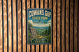 a vintage metal sign for Cowans Gap State Park in Pennsylvania, with a scenic landscape of mountains, trees, and a rocky outcropping.