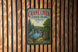 A vintage metal sign for Crane Creek State Park in Ohio, featuring a scenic illustration of a lake, trees, and a bird, mounted on a wooden wall.