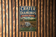 A vintage metal sign for Crater of Diamonds State Park in Arkansas, featuring a diamond and a building in the background.