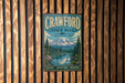 A metal sign for Crawford State Park in Washington, featuring a scenic mountain landscape with a river and pine trees.