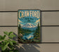 A vintage metal sign for Crawford State Park in Washington, featuring a scenic mountain landscape with pine trees, a lake, and a waterfall.