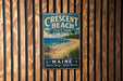 A vintage metal sign for Crescent Beach State Park in Maine, featuring a beach scene with a lighthouse and mountains in the background.