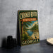 A vintage-style metal sign for Crooked River State Park in Georgia, featuring a scenic illustration of a river and forest landscape.