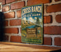 A vintage metal sign for Cross Ranch State Park in North Dakota, featuring a scenic landscape with mountains, a river, and a signpost.