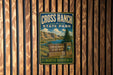 A vintage metal sign for Cross Ranch State Park in North Dakota, featuring a scenic landscape with mountains, a river, and a pine tree.