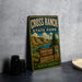 A vintage-style metal sign for Cross Ranch State Park in North Dakota, featuring a scenic landscape with mountains, a river, and a sign welcoming visitors to the park.